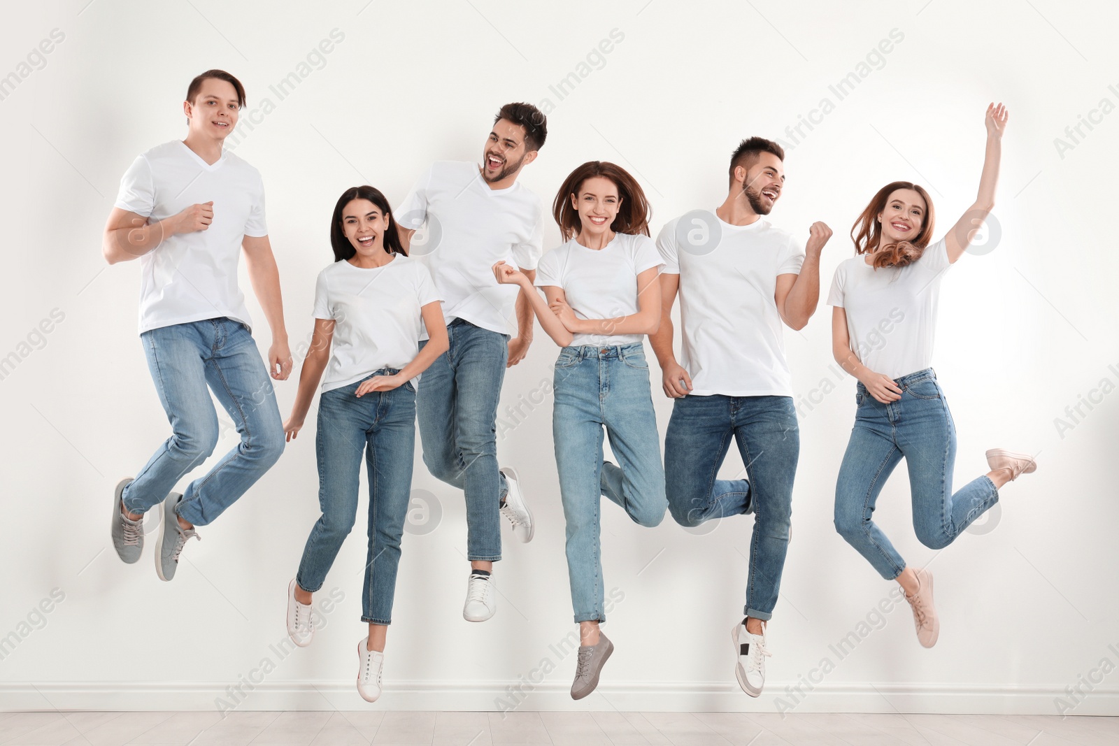 Photo of Group of young people in stylish jeans jumping near white wall