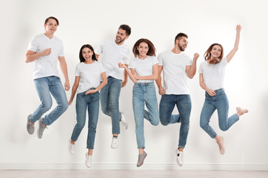 Photo of Group of young people in stylish jeans jumping near white wall