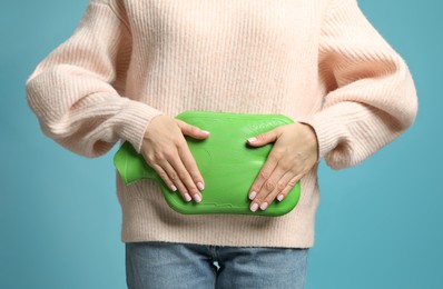 Photo of Woman using hot water bottle to relieve menstrual pain on light blue background, closeup