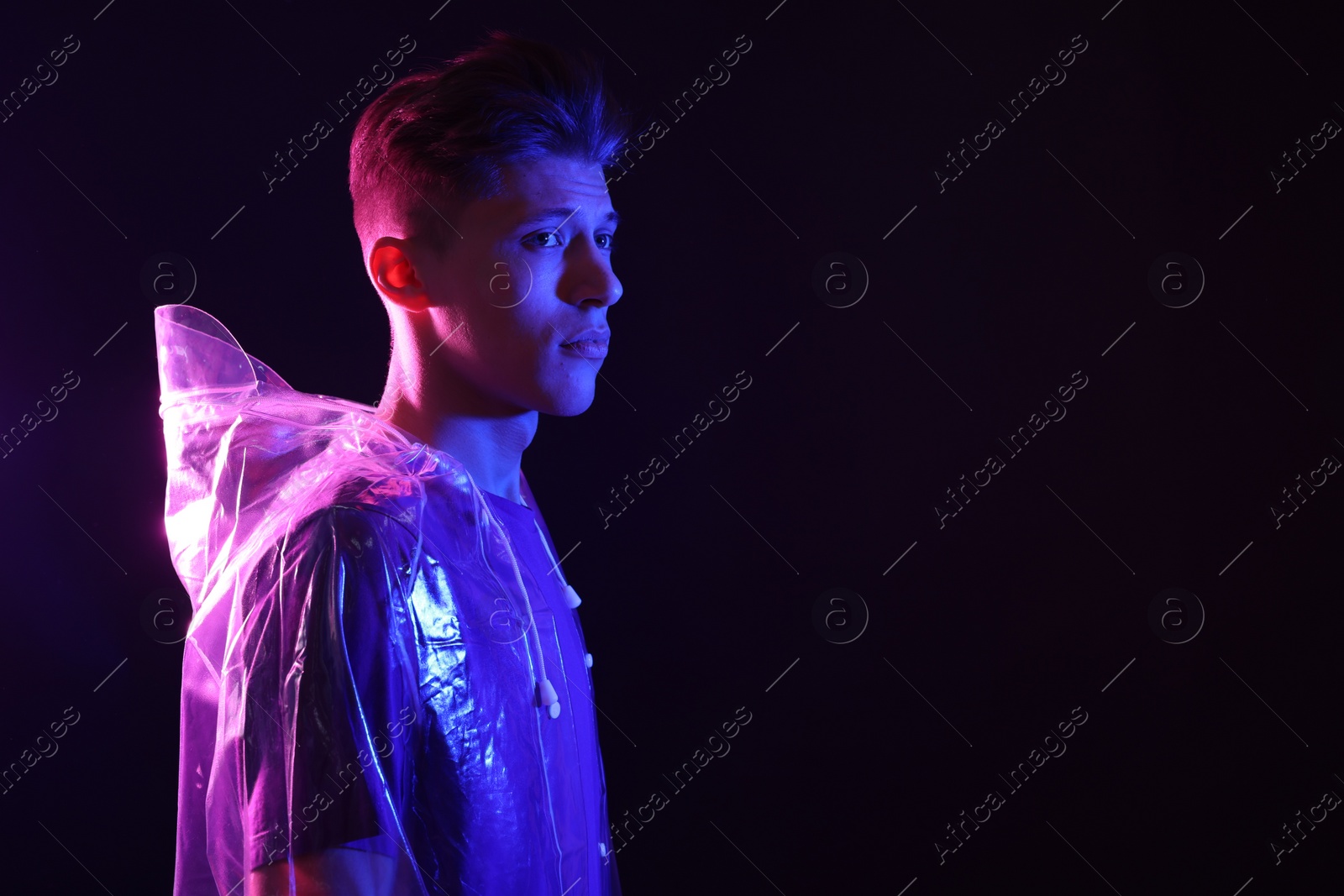 Photo of Young man wearing clear coat on dark background in neon lights. Space for text