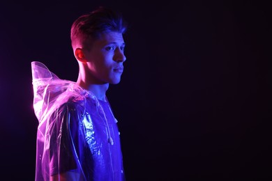 Photo of Young man wearing clear coat on dark background in neon lights. Space for text