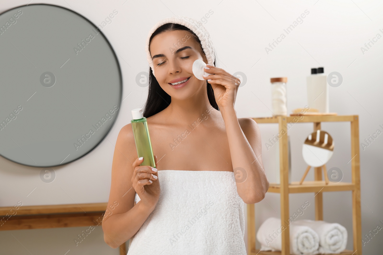 Photo of Young woman using cotton pad with micellar water indoors