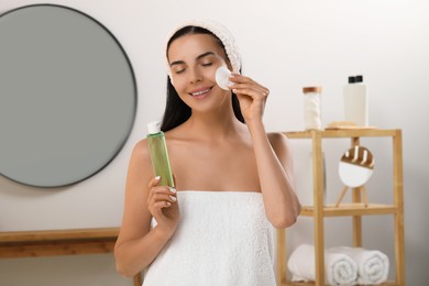 Photo of Young woman using cotton pad with micellar water indoors