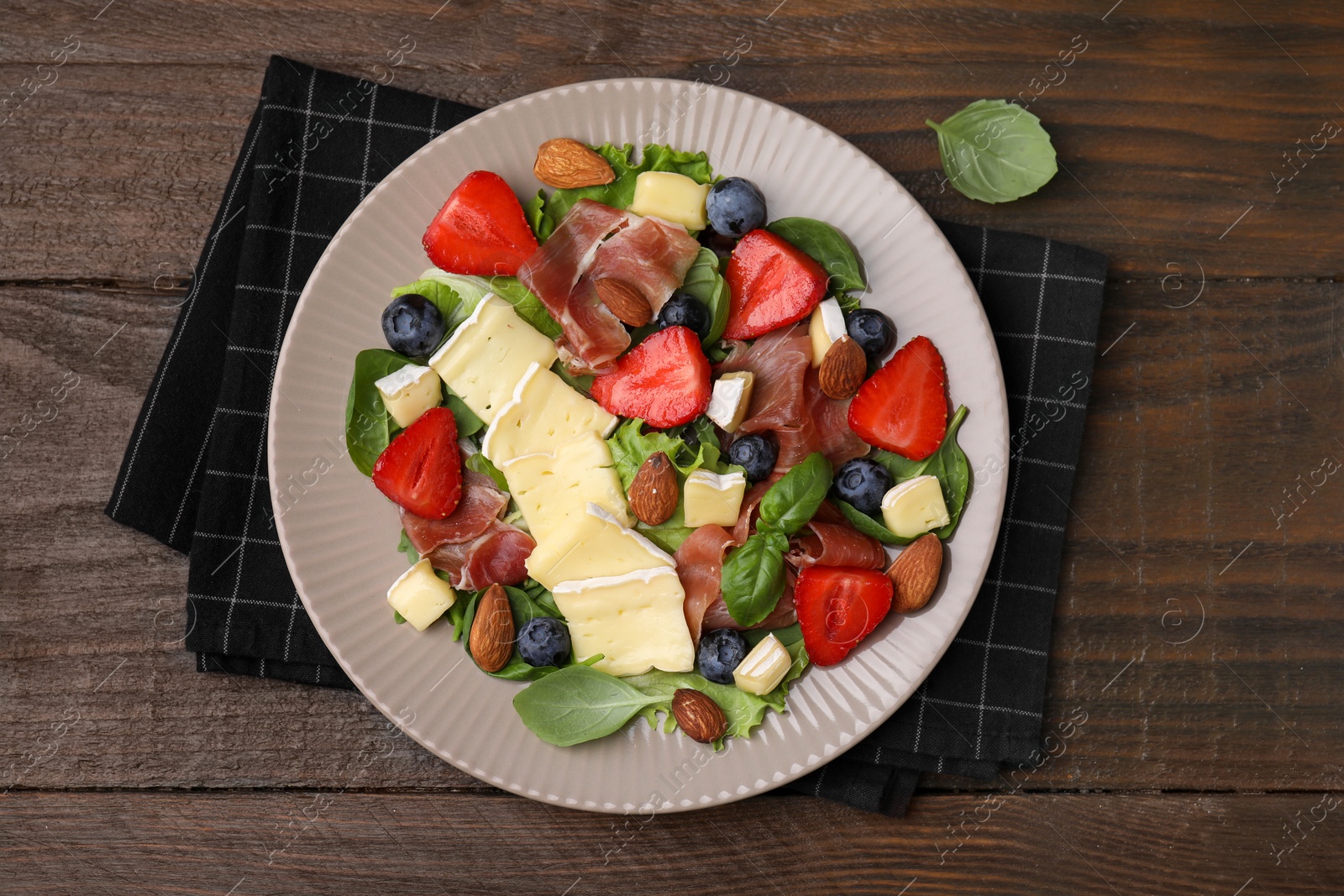 Photo of Tasty salad with brie cheese, prosciutto, almonds and berries on wooden table, top view