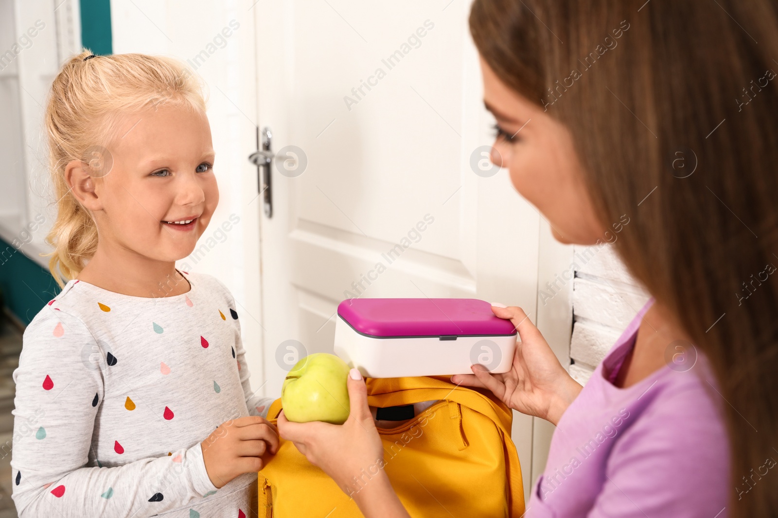 Photo of Young mother and little child putting lunch into school bag at home