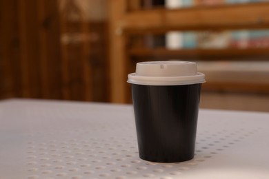 Takeaway paper cup with plastic lid on white table indoors, space for text