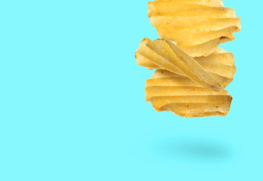 Image of Tasty ridged potato chips falling on cyan background, space for text
