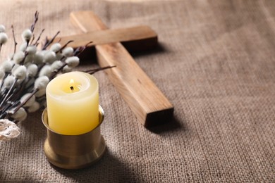 Photo of Burning church candle, wooden cross and willow branches on beige cloth, space for text
