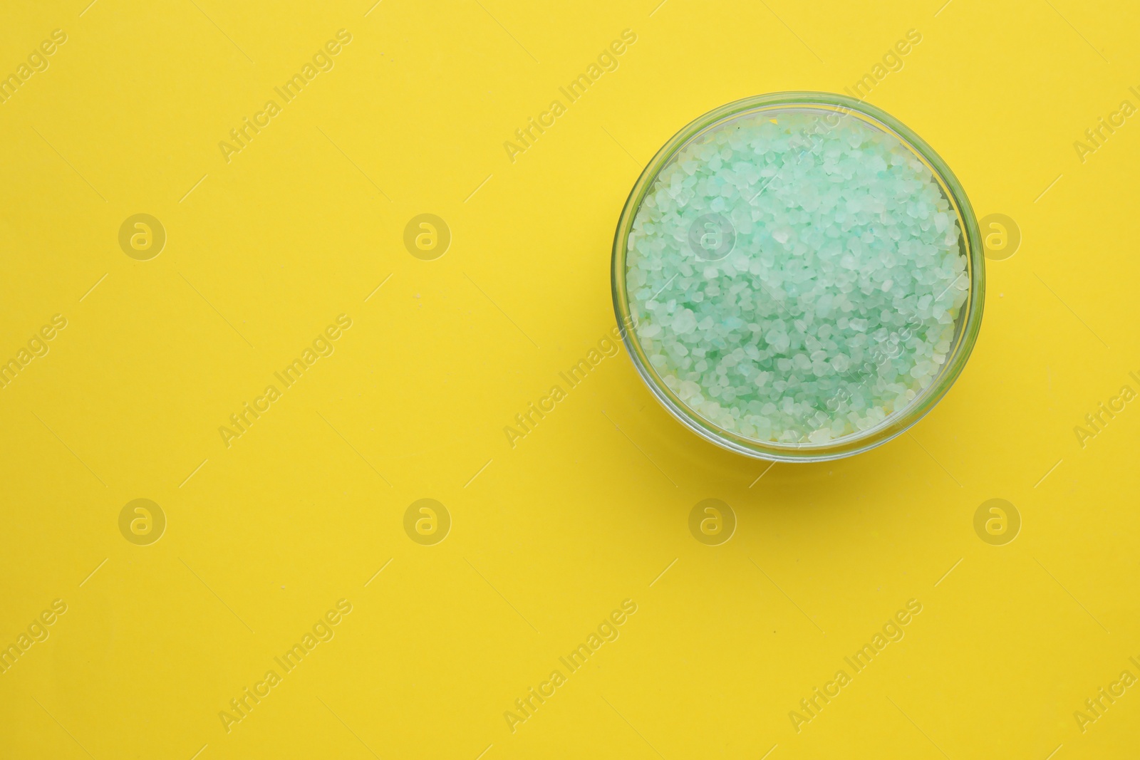 Photo of Bowl with turquoise sea salt on yellow background, top view. Space for text