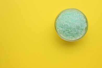 Photo of Bowl with turquoise sea salt on yellow background, top view. Space for text