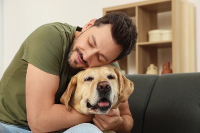 Photo of Man hugging his cute Labrador Retriever on sofa at home. Space for text