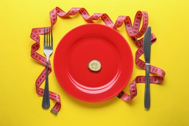 Photo of Plate with cucumber slice, cutlery and measuring tape on yellow background, flat lay. Diet concept