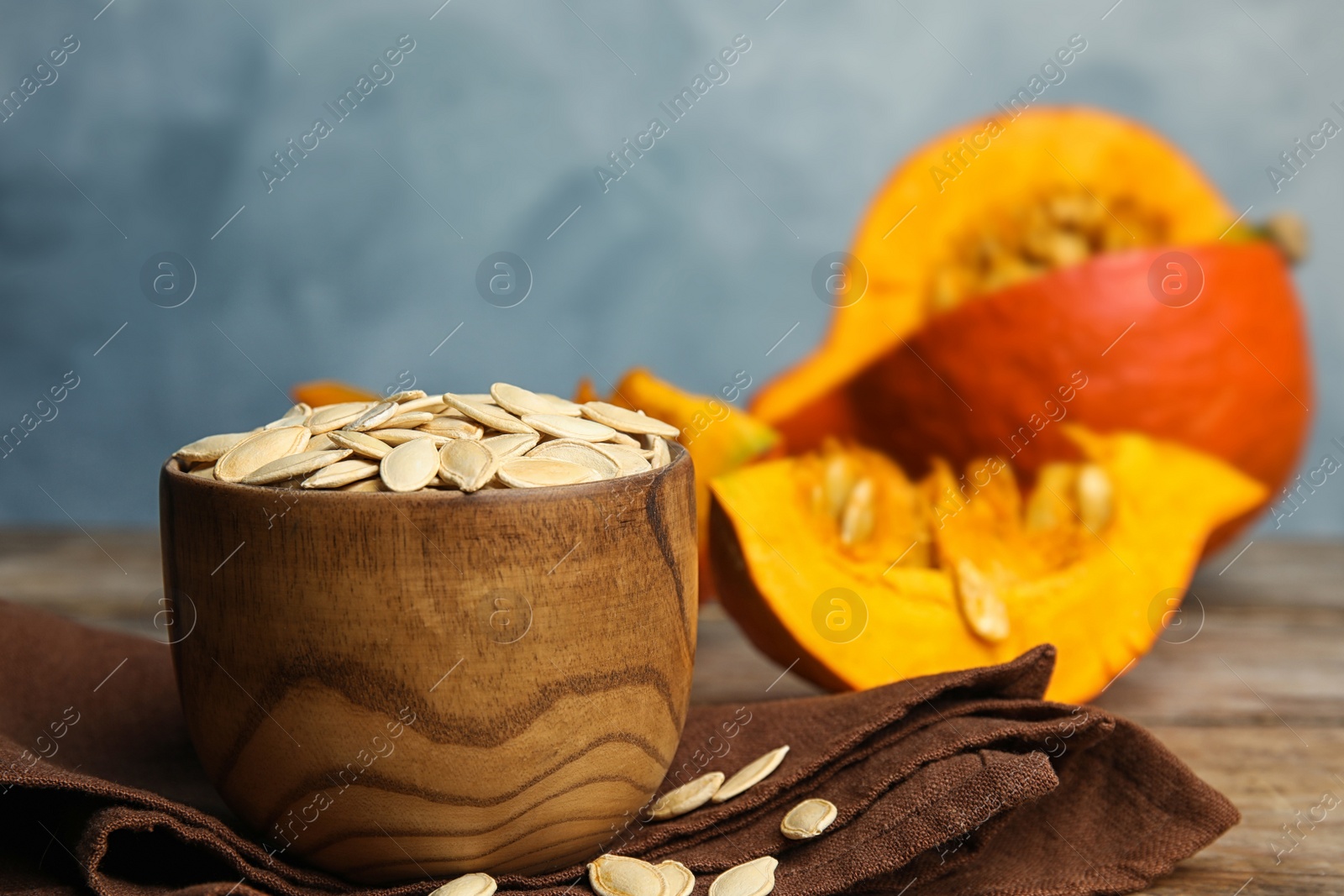 Photo of Bowl of raw unpeeled pumpkin seeds on wooden table against blue background. Space for text