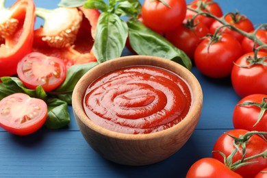 Photo of Bowl of tasty ketchup and ingredients on blue wooden table, closeup