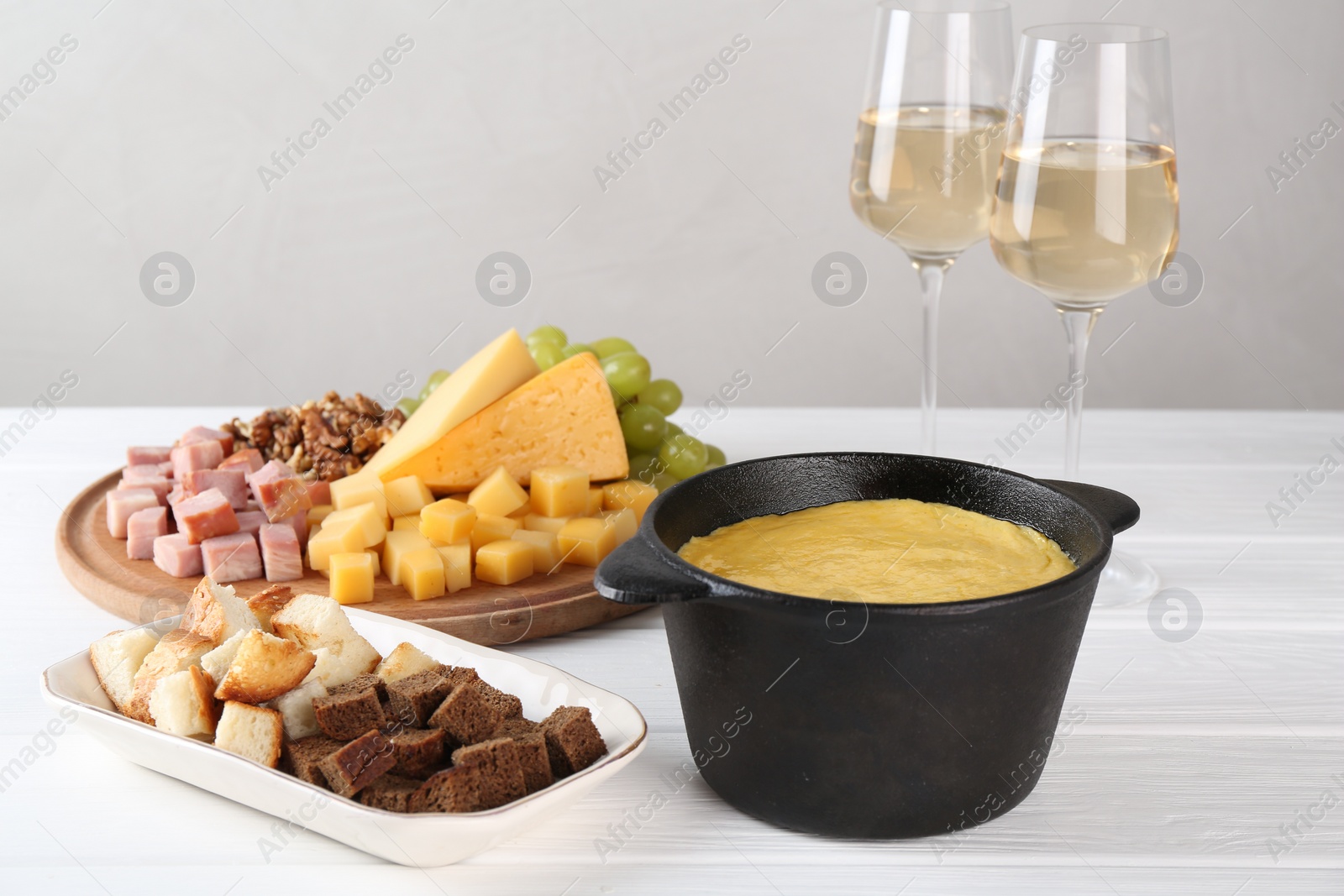 Photo of Fondue with tasty melted cheese, different products and aromatic wine in glasses on white wooden table