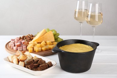 Fondue with tasty melted cheese, different products and aromatic wine in glasses on white wooden table