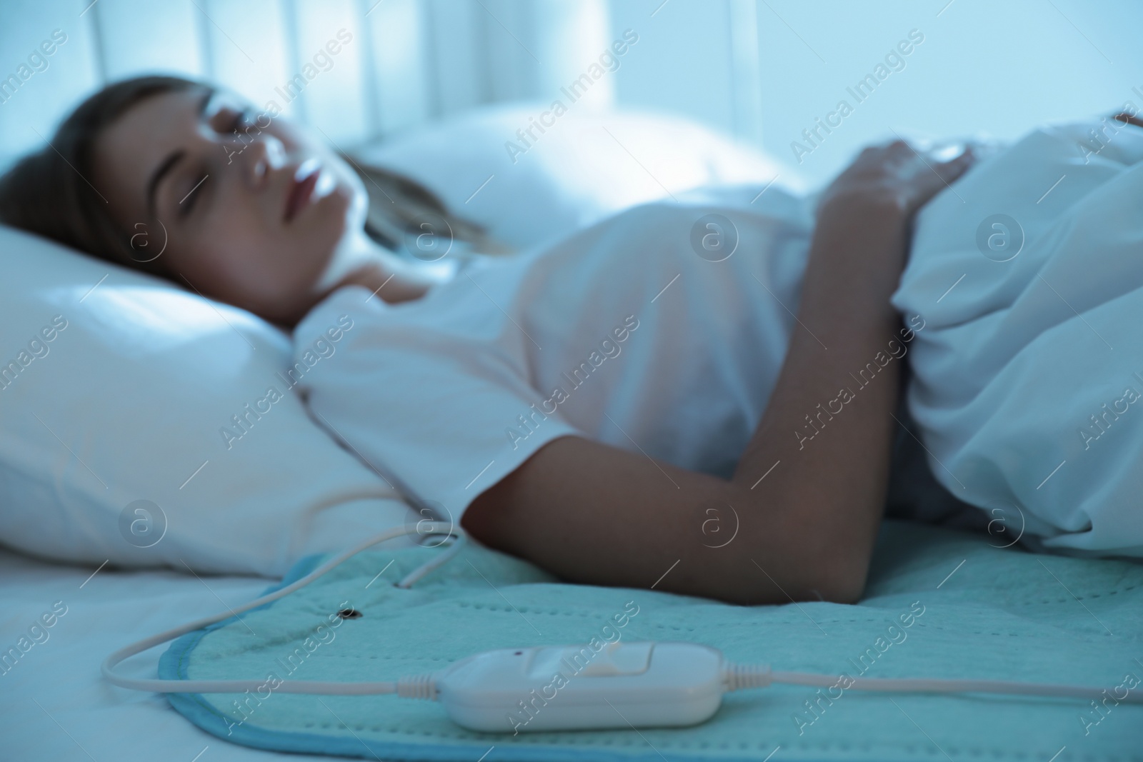 Photo of Young woman sleeping in bed with electric heating pad, focus on cable