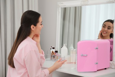 Photo of Woman getting ready at dressing table with cosmetic refrigerator indoors