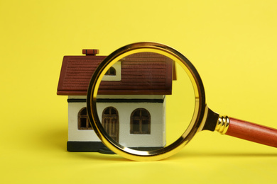 House model and magnifying glass on yellow background. Search concept