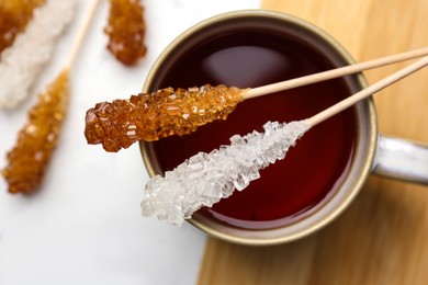 Sticks with sugar crystals and cup of tea on table, top view