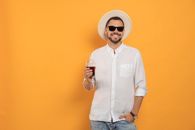 Photo of Man holding plastic cup of delicious juice on orange background, space for text