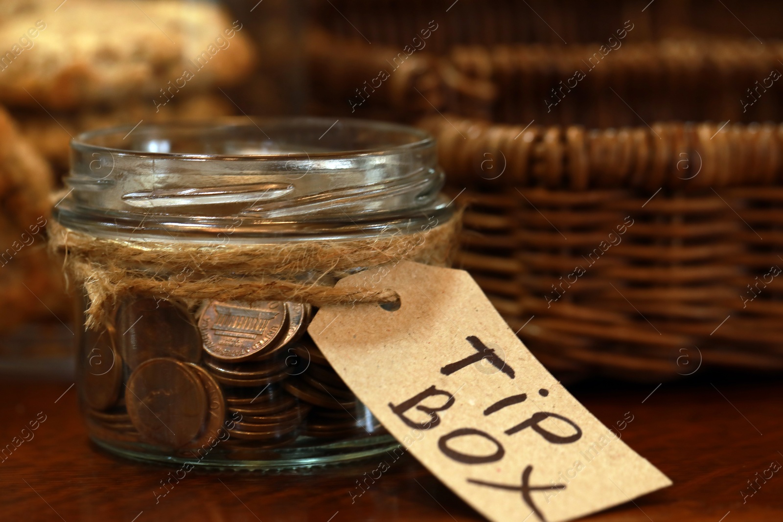 Photo of Tip box full of coins on wooden table in cafe, closeup