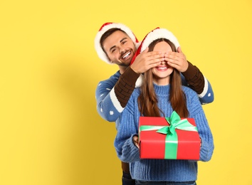 Couple wearing Christmas sweaters and Santa hats on yellow background