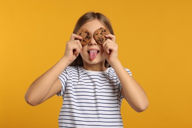 Photo of Girl covering eyes with chocolate chip cookies and showing tongue on orange background