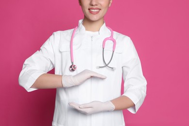 Photo of Young doctor holding something on pink background, closeup