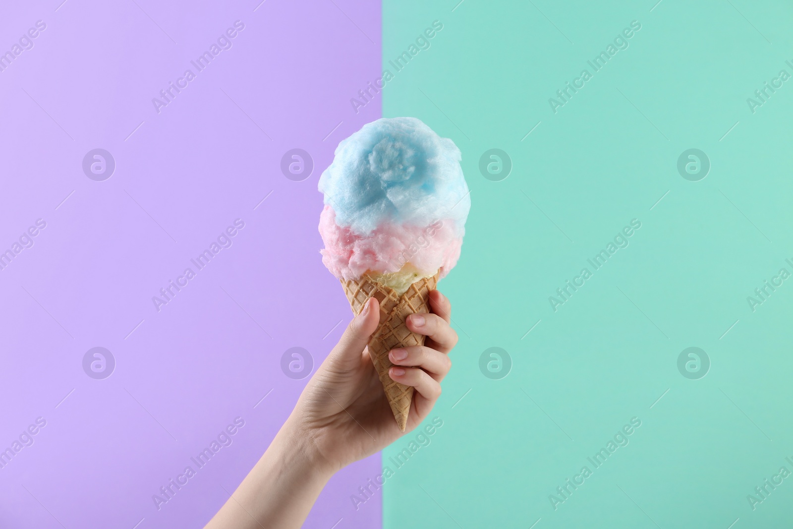 Photo of Woman holding waffle cone with cotton candy on color background, closeup