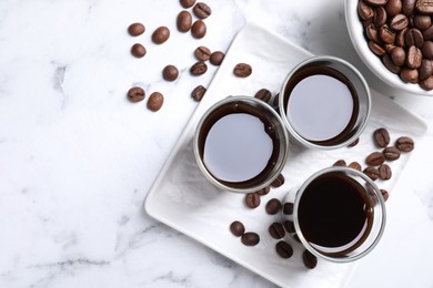 Photo of Glasses of coffee liqueur and beans on white marble table, flat lay. Space for text