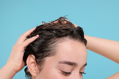 Photo of Woman washing hair on light blue background, closeup