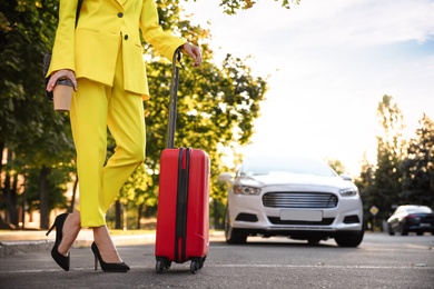 Photo of Woman with suitcase waiting for taxi on city street, closeup