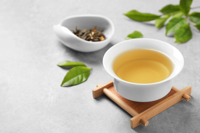 Photo of Cup of green tea, dry and fresh leaves on grey table. Space for text
