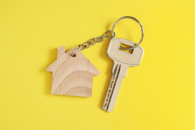 Key with keychain in shape of house on yellow background, top view