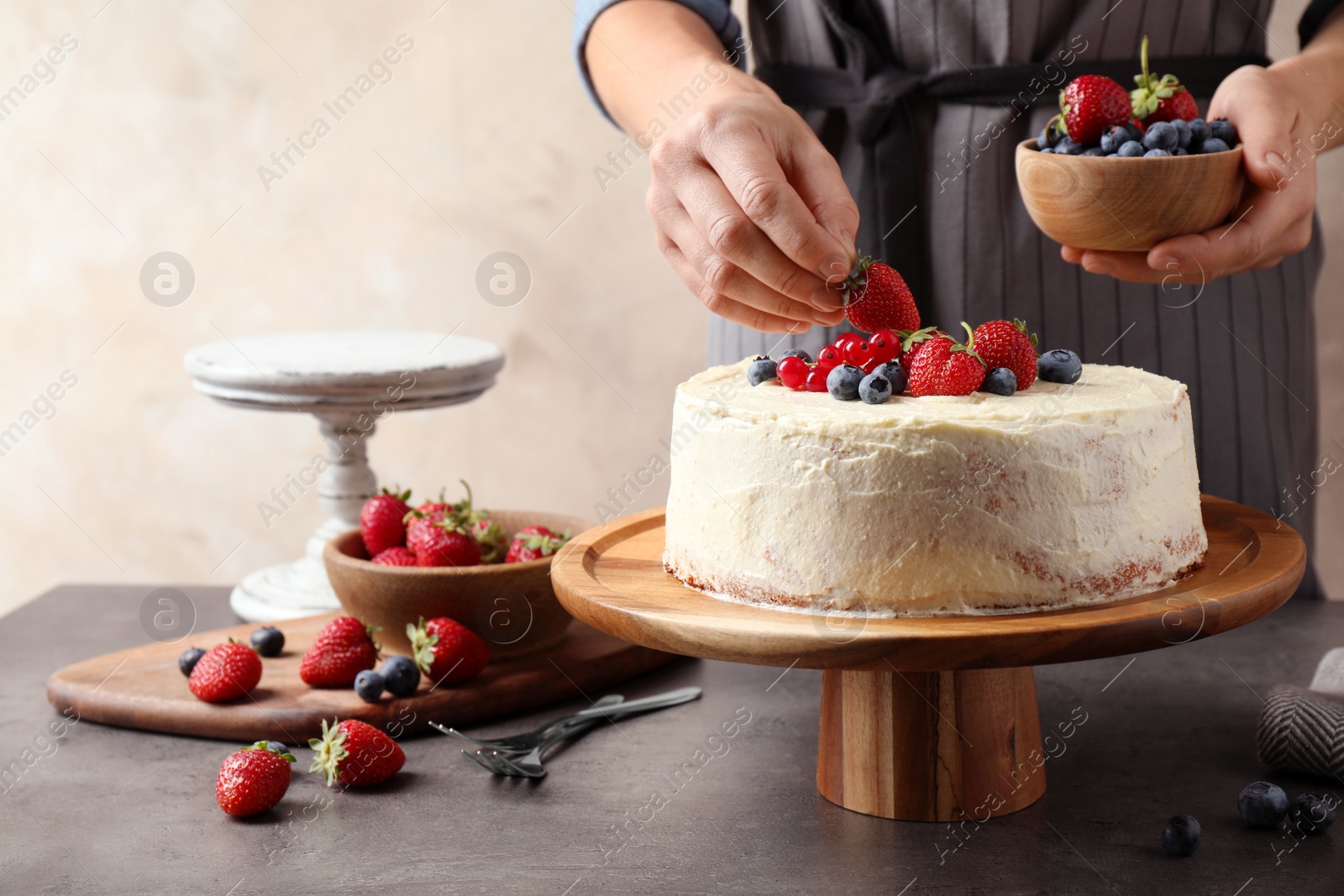 Photo of Woman decorating delicious homemade cake with fresh berries at table indoors, closeup