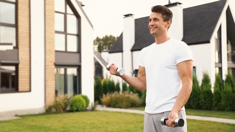 Sporty man doing exercise with dumbbells on backyard. Healthy lifestyle