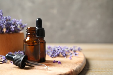 Photo of Bottles of essential oil and lavender flowers on wooden table. Space for text