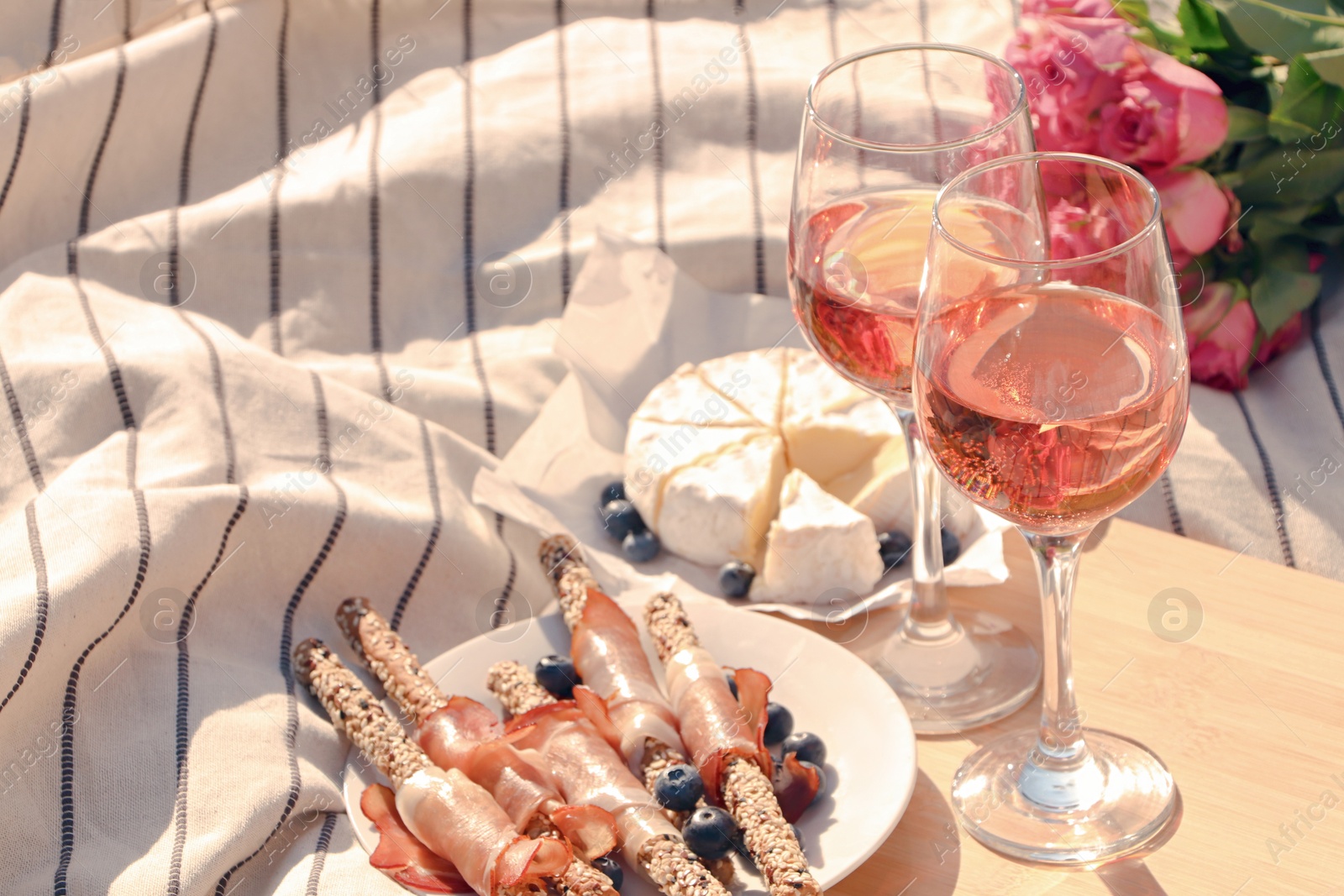 Photo of Glasses of delicious rose wine, flowers and food on picnic blanket outdoors