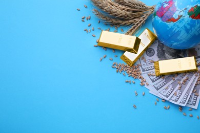 Photo of Import and export concept. Globe, ears of wheat, banknotes and gold bars on light blue background, flat lay. Space for text