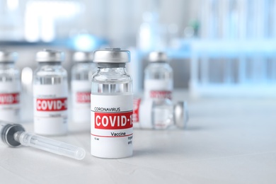 Photo of Glass vials with COVID-19 vaccine and syringe on light table. Space for text