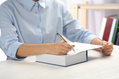 Photo of Writer signing autograph in book at table, closeup