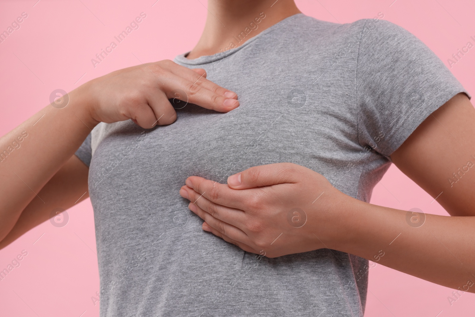 Photo of Woman doing breast self-examination on pink background, closeup