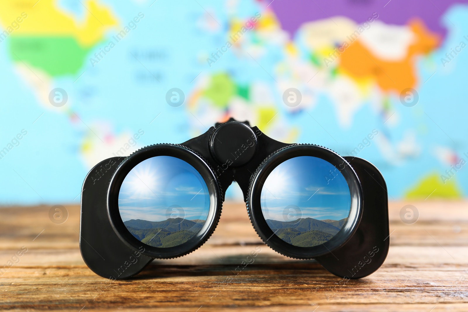 Image of Binoculars on wooden table against blurred map. Mountain landscape reflecting in lenses