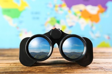 Binoculars on wooden table against blurred map. Mountain landscape reflecting in lenses