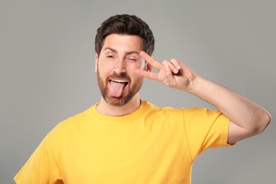 Photo of Man showing his tongue and V-sign on gray background