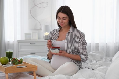 Photo of Pregnant woman eating breakfast on bed at home. Healthy diet