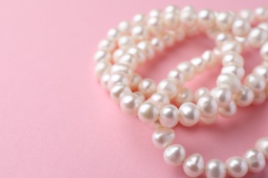 Elegant necklace with pearls on pink background, closeup. Space for text