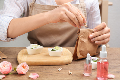 Woman holding paper bag with natural handmade soap at wooden table, closeup
