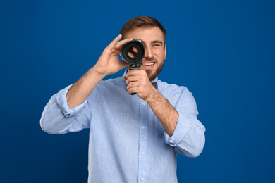 Young man using vintage video camera on blue background